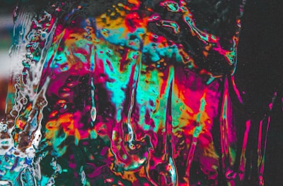 A vibrant and abstract composition with swirling patterns and a mix of bright colors including pink, blue, orange, and yellow. The colors blend and overlap, creating an effect reminiscent of oil on water or stained glass. Light reflects and refracts across the surface, giving a dynamic and lively feel.