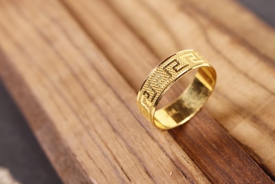 A shining gold ring with delicate engravings resting on a polished wooden surface.