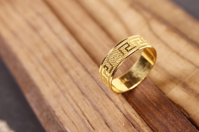Close-up of a sleek geometric gold ring resting on a smooth white marble surface.