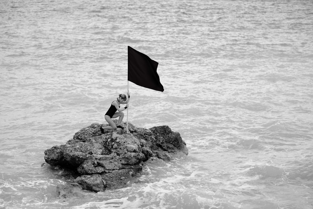 昼間、水辺の岩の上に立つ旗を持つ人