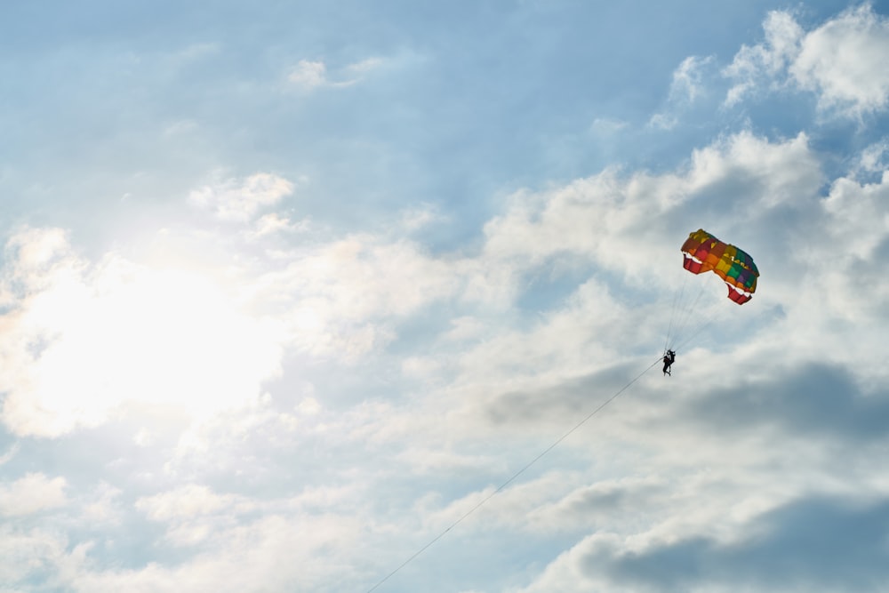 person in red and yellow parachute under white clouds and blue sky during daytime