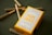 A yellow box labeled 'MOM GRASS' containing five pre-rolled 100% organic hemp flower joints is displayed on a dark surface. Several pre-rolled joints are scattered around the box.