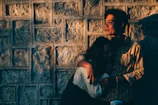 An intimate moment of a couple embracing near a charcoal-colored rustic wall glowing in warm light.