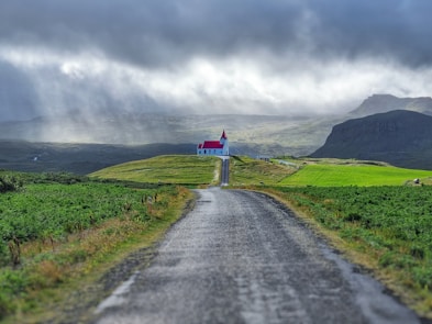 gray asphalt road between green grass field under gray cloudy sky during daytime