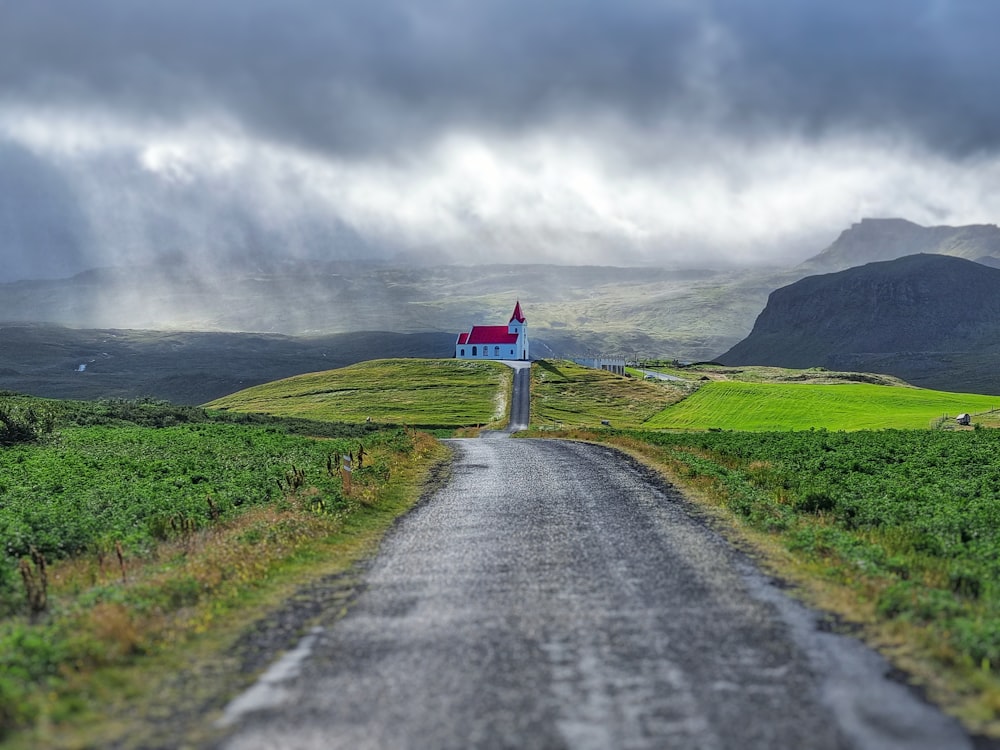 estrada de asfalto cinza entre campo de grama verde sob céu nublado cinza durante o dia