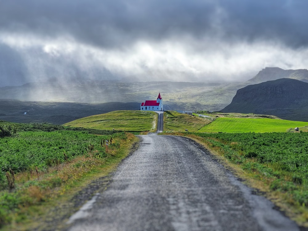 gray asphalt road between green grass field under gray cloudy sky during daytime