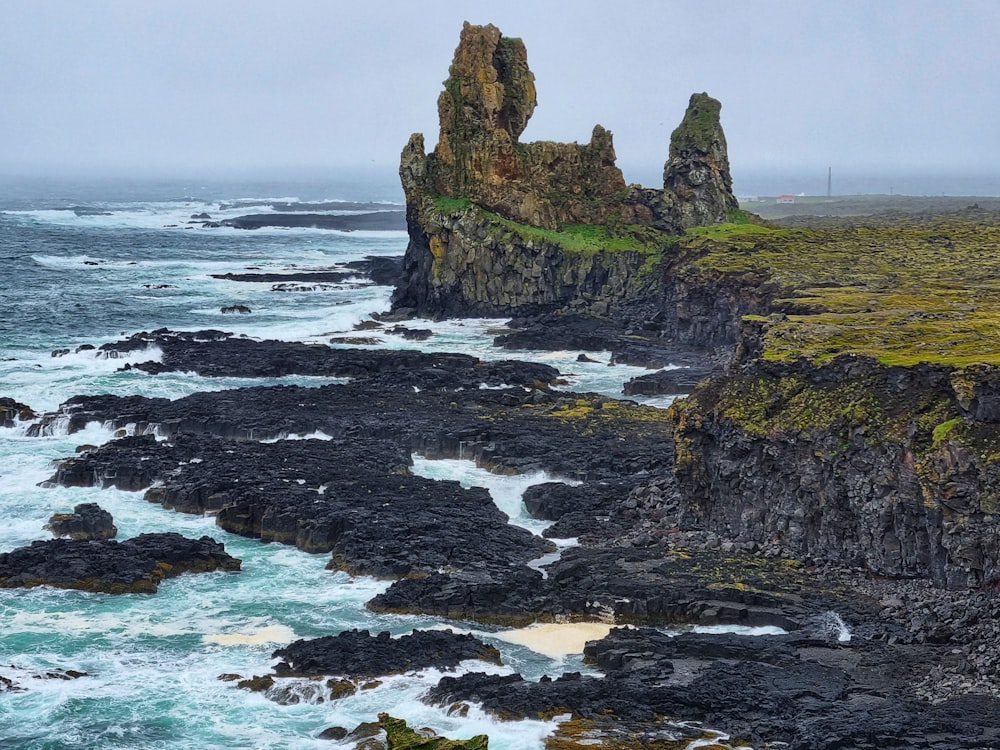 formação rochosa marrom e verde no mar durante o dia