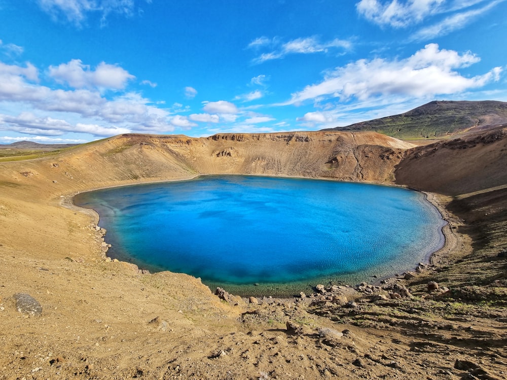 blue lake surrounded by brown and green mountains under blue sky during daytime