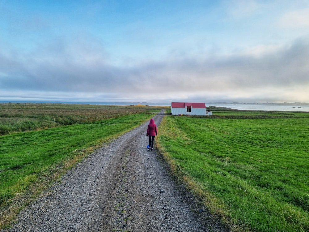 person in pink jacket walking on pathway between green grass field under blue sky during daytime