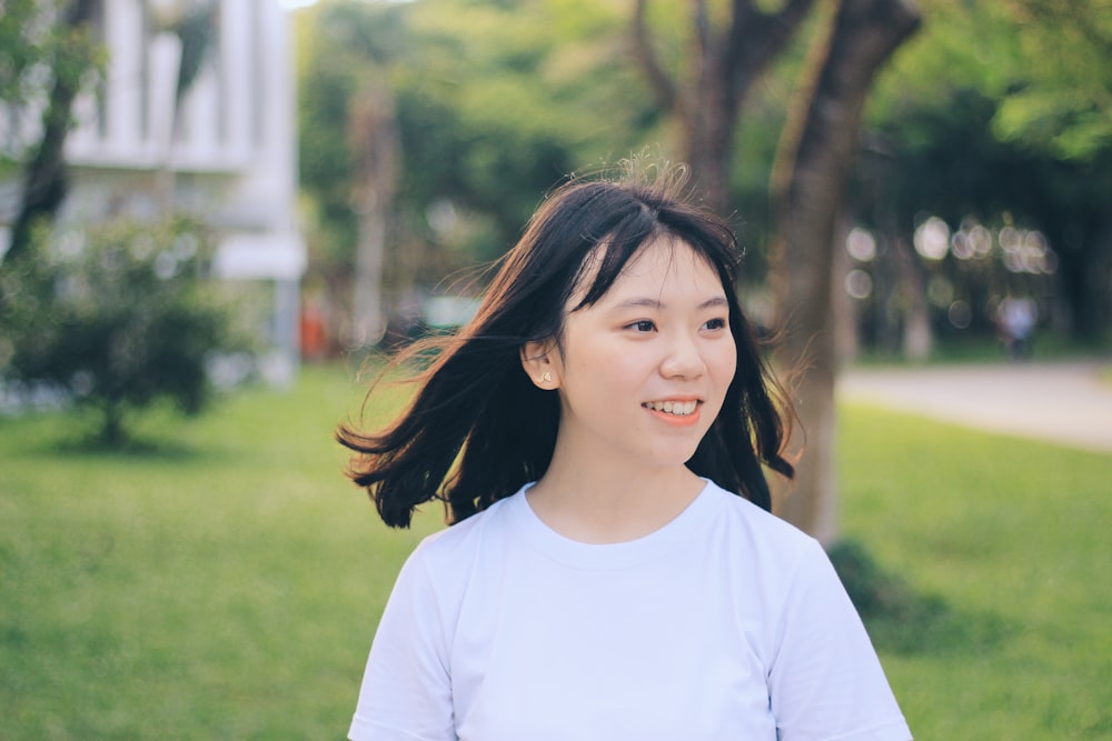 girl in white crew neck t-shirt standing on green grass field during daytime