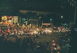 Nighttime shot of a glowing banner biker weaving through a crowd at an outdoor event.
