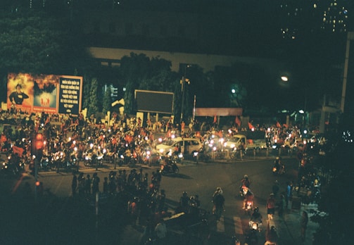 Nighttime shot of a glowing banner biker weaving through a crowd at an outdoor event.
