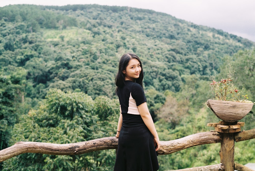 woman in black dress standing on tree branch during daytime