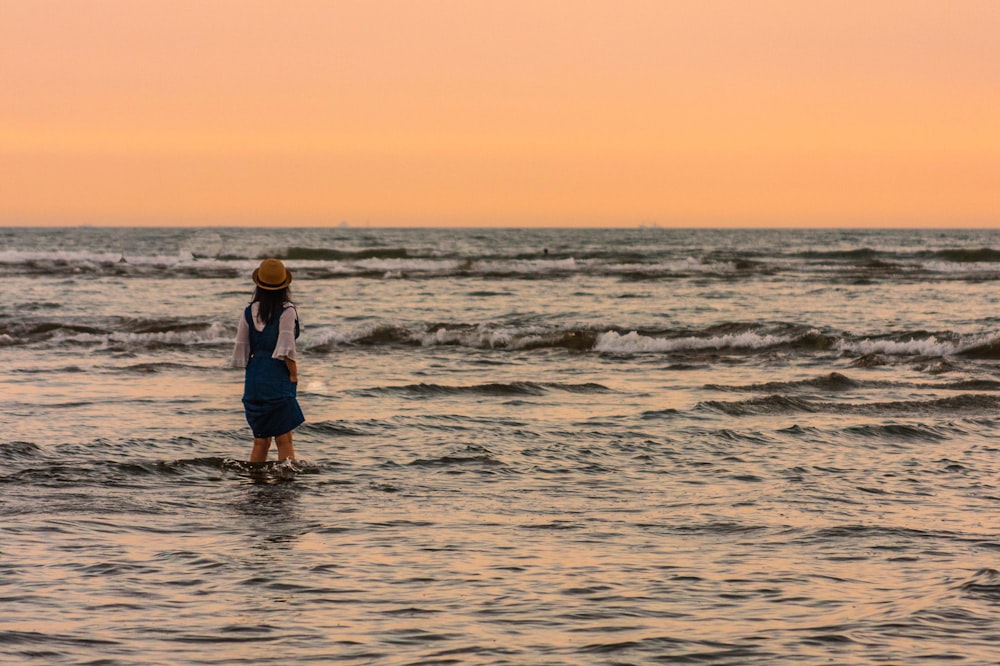 man in blue shirt and black shorts standing on sea shore during sunset