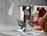 A close-up view of a sewing machine with hands guiding fabric under the presser foot. The needle is prominently in focus, indicating an active sewing process.