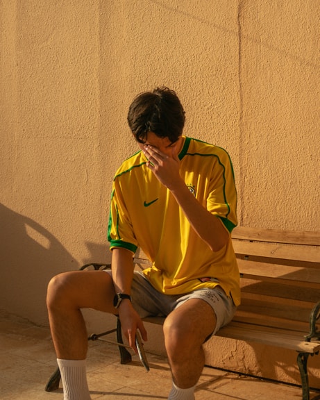 man in yellow crew neck t-shirt sitting on brown wooden bench
