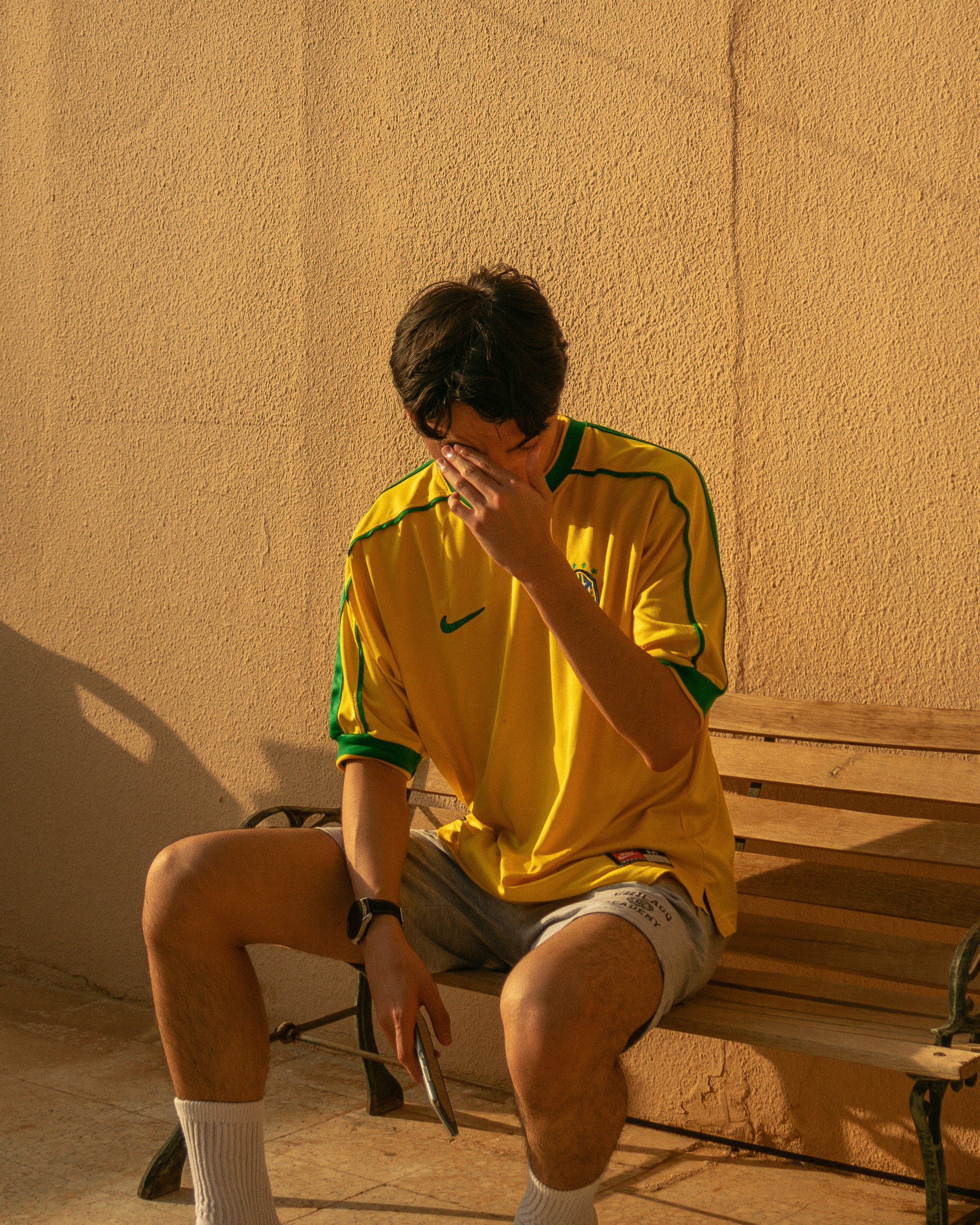 man in yellow crew neck t-shirt sitting on brown wooden bench