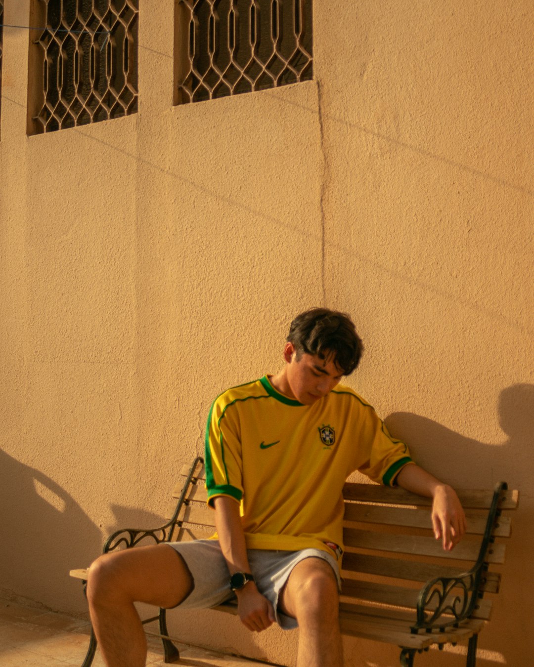 man in green polo shirt sitting on brown wooden bench