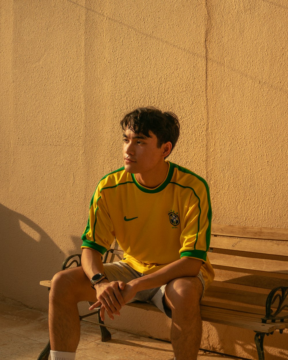man in green nike soccer jersey sitting on brown wooden bench