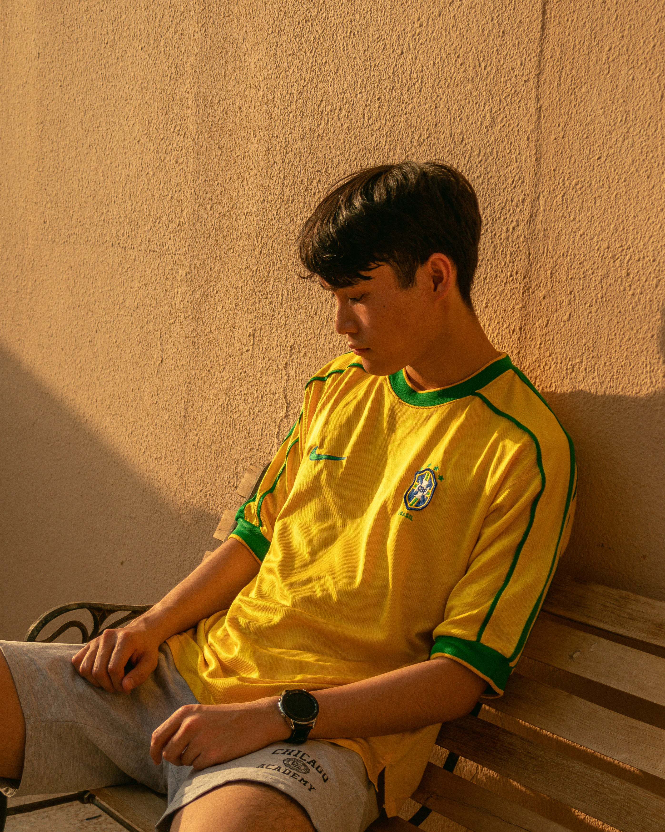 boy in green adidas crew neck t-shirt sitting on brown wooden bench