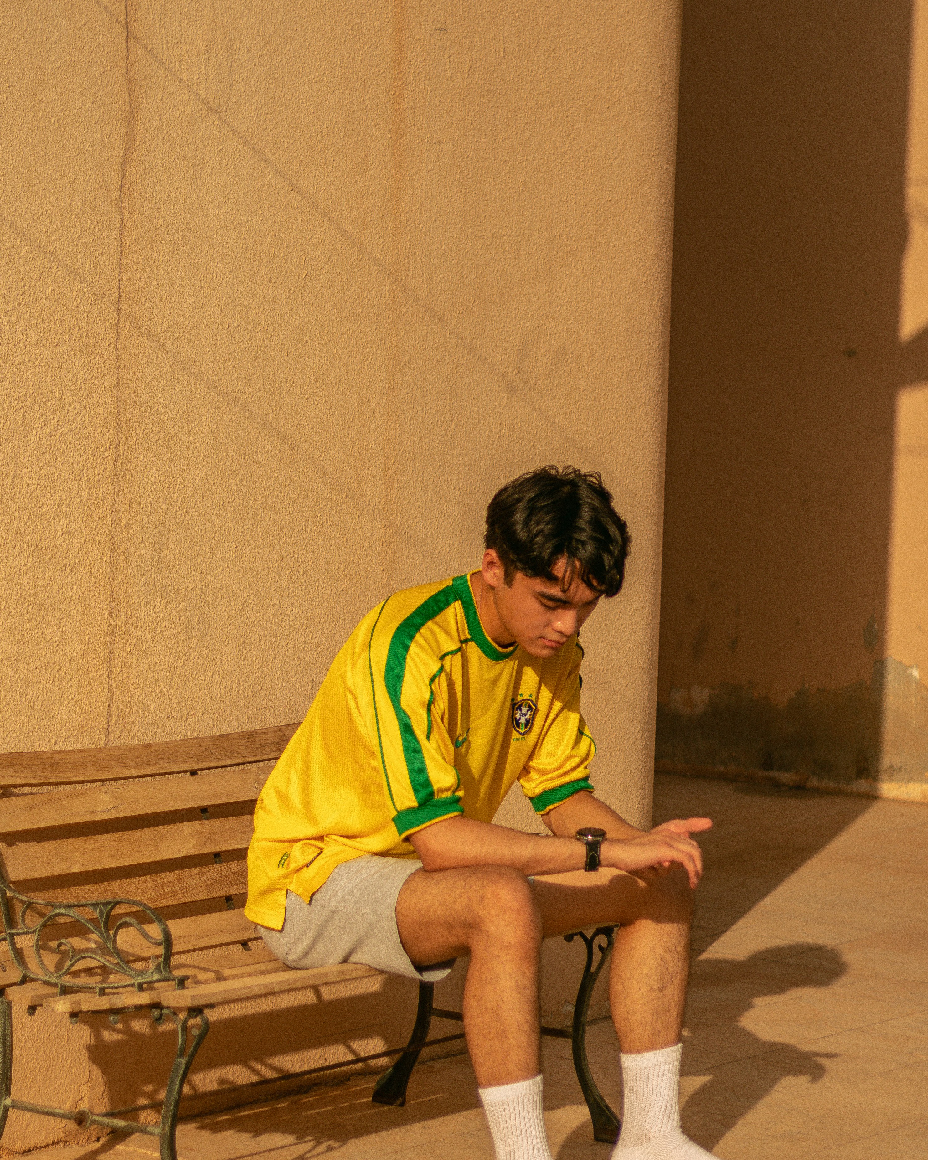 man in green and yellow adidas shirt sitting on brown wooden bench