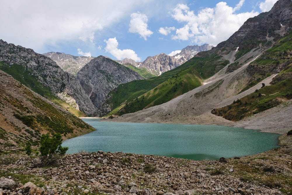 green lake surrounded by mountains under blue sky during daytime