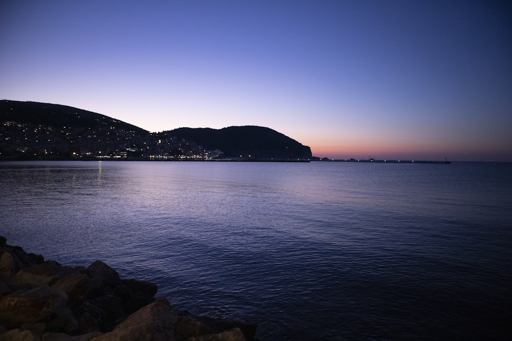 body of water near mountain during sunset