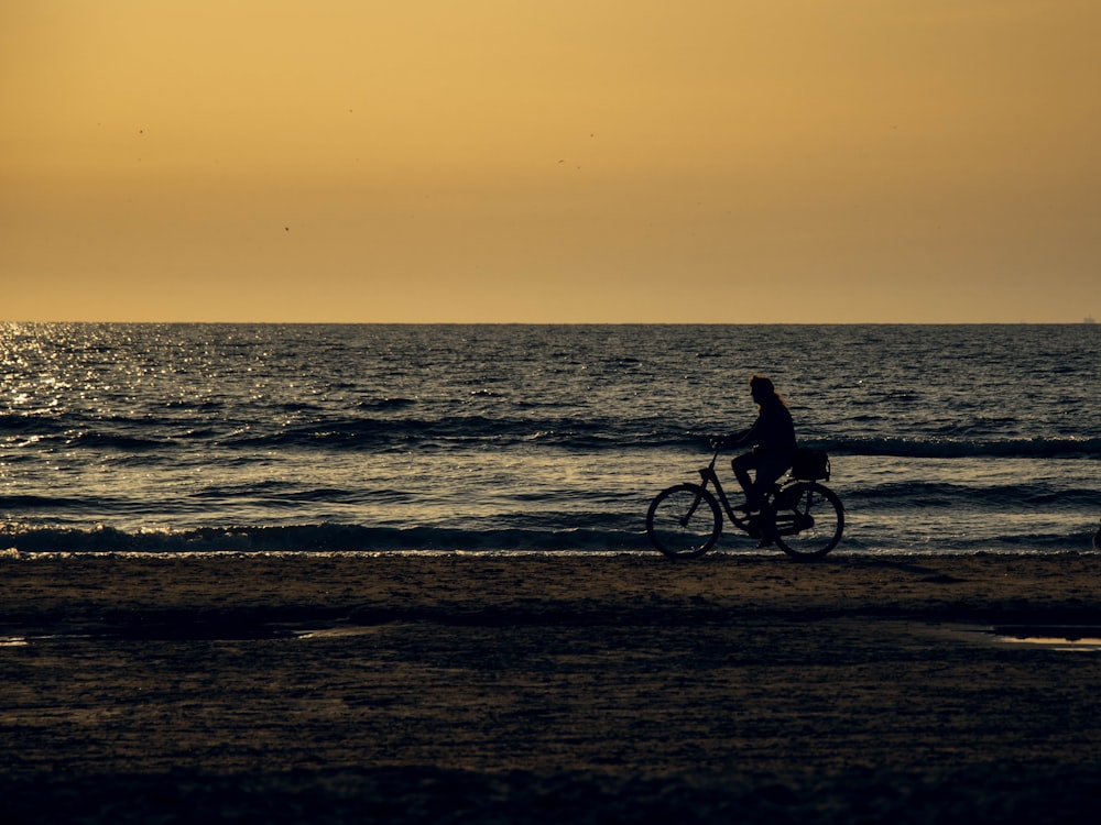 silhouette of person riding bicycle on beach during sunset