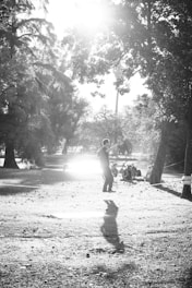 grayscale photo of woman sitting on concrete bench near trees