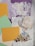 Various craft materials are arranged, including lace fabric, doilies, pastel paper cards, aged text paper squares, and floral cutouts. The lace and doilies display intricate patterns, the paper is pale and weathered, and the floral designs feature vibrant colors against a soft backdrop.