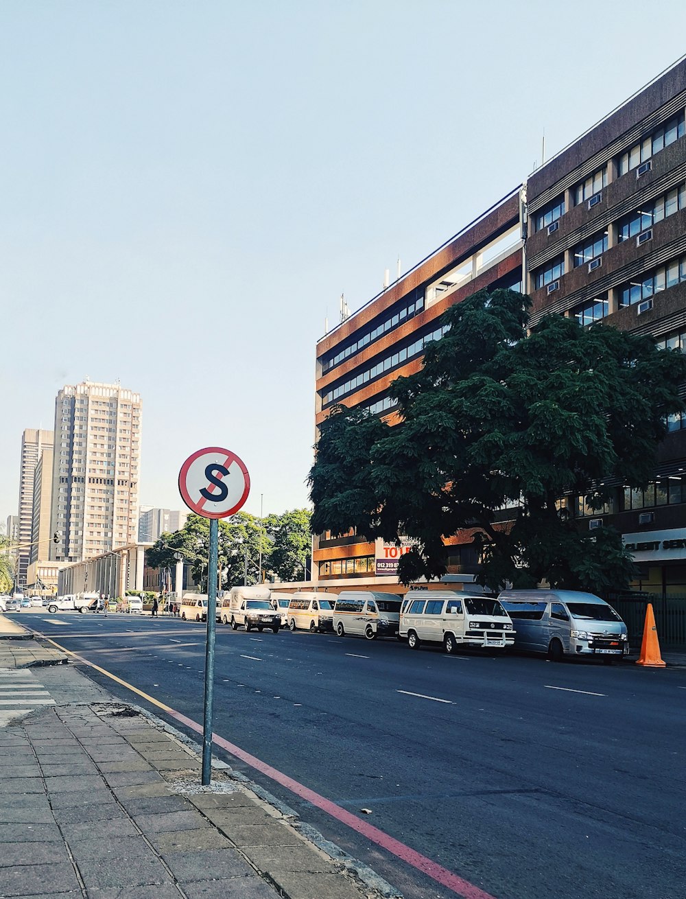 cars parked on side of the road near high rise buildings during daytime