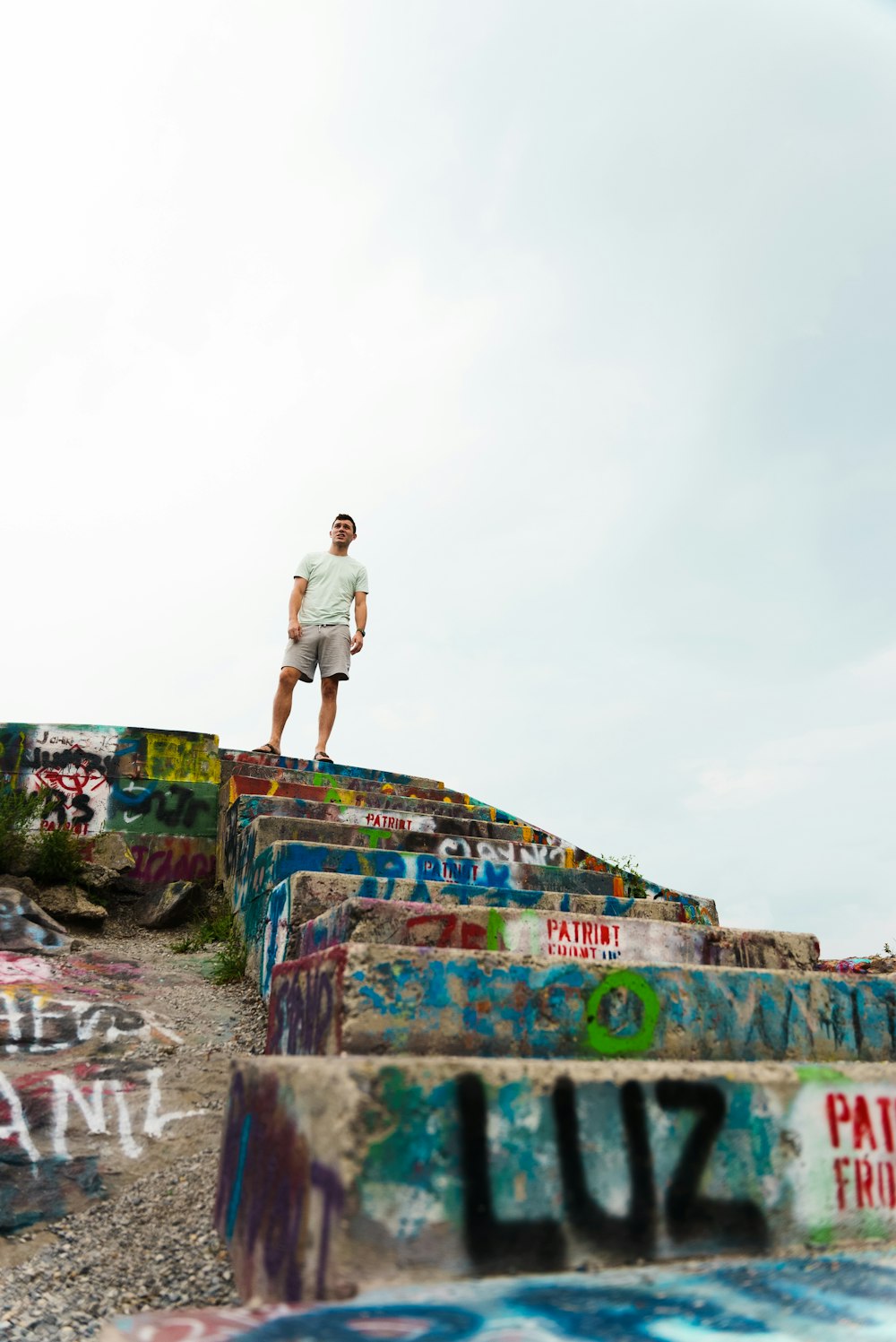 man in white t-shirt and gray shorts standing on concrete wall during daytime