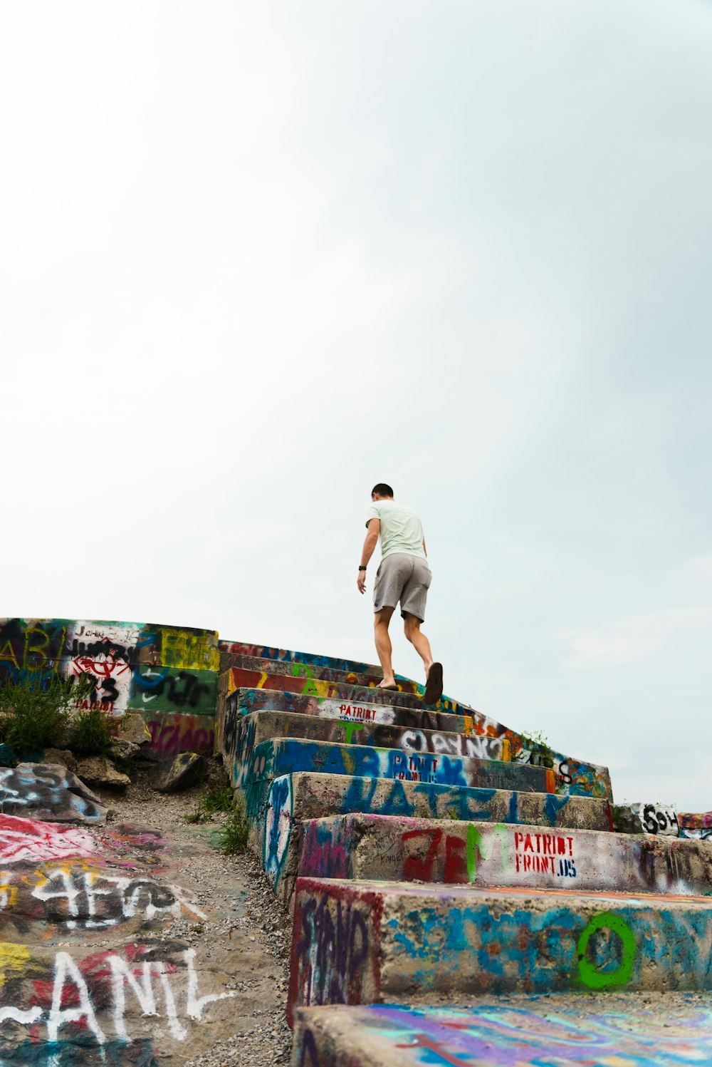 man in white t-shirt and brown shorts standing on rock formation during daytime