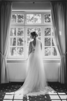 A serene portrait of the bride gazing out a window, bathed in natural light with a hint of royal purple in the background.
