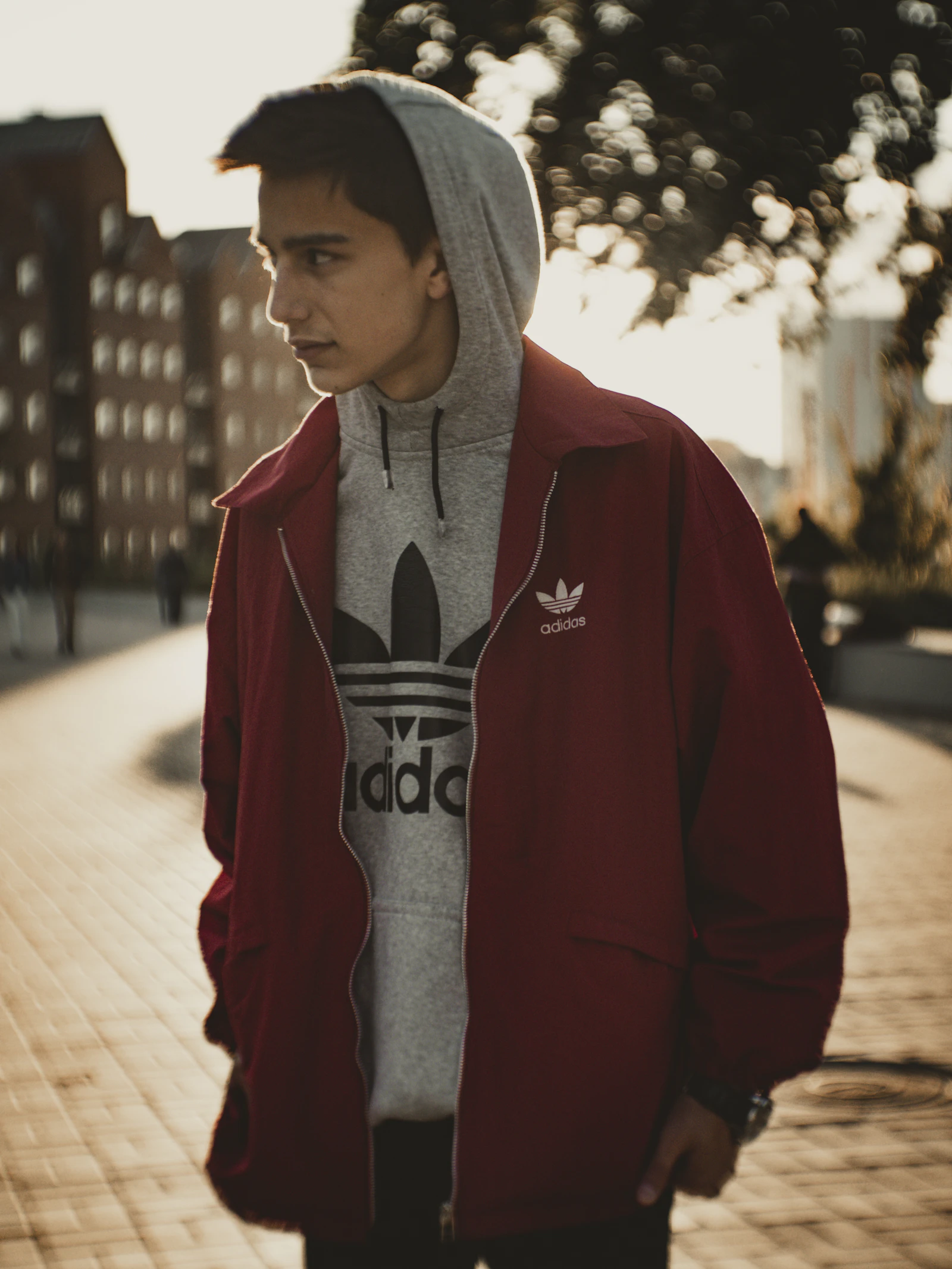 Person wearing a red pullover hoodie with a kangaroo pocket and drawcord hood, standing outdoors on a sidewalk