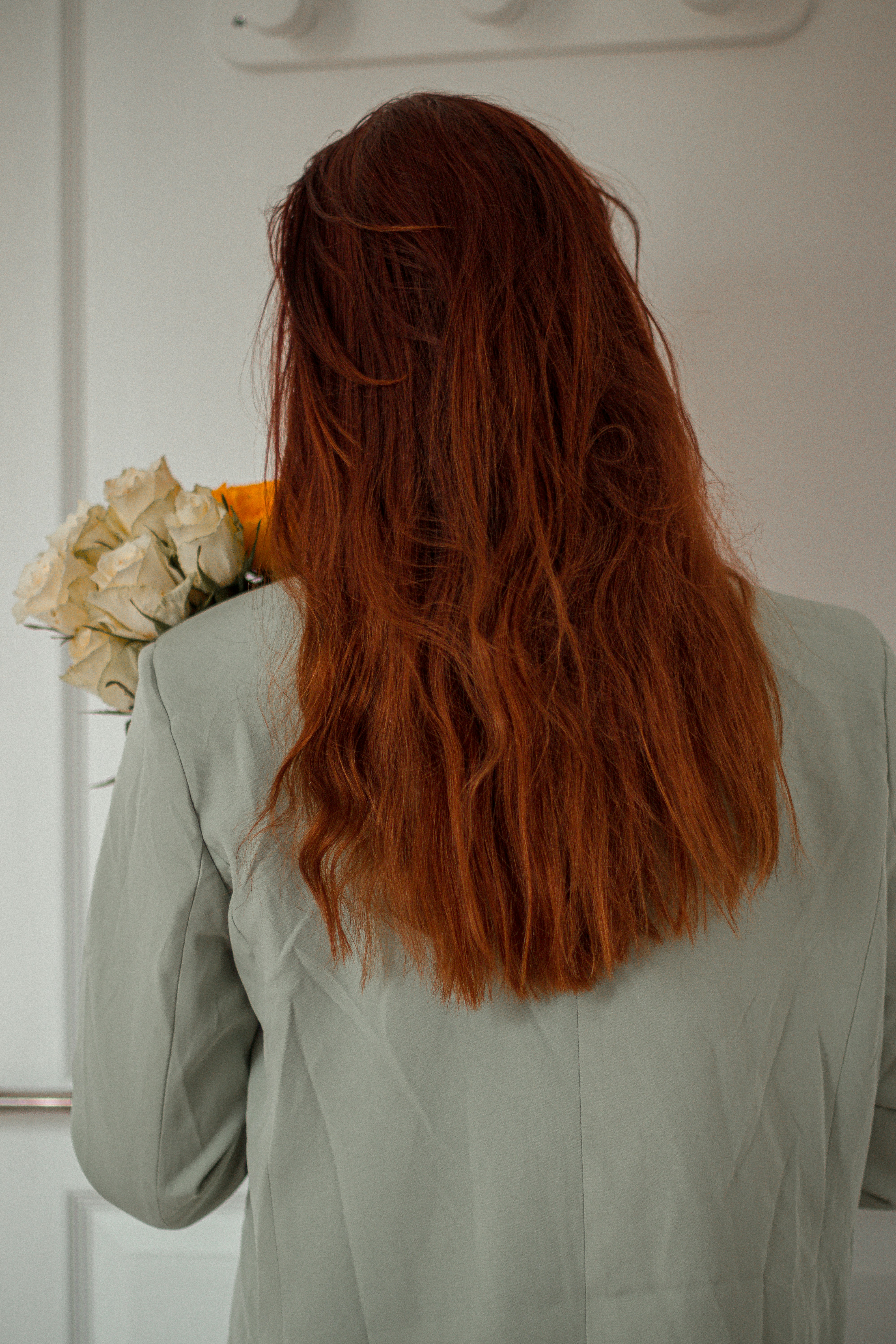 Woman with naturally tousled red hair holding white roses behind her back