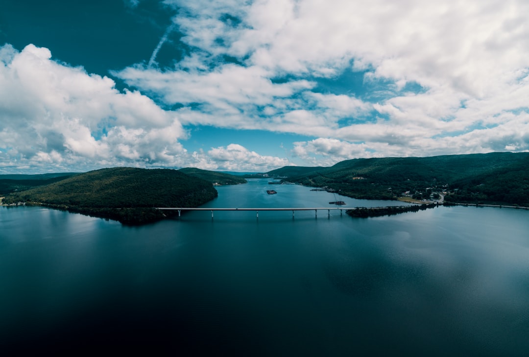 green mountains beside body of water under white clouds and blue sky during daytime