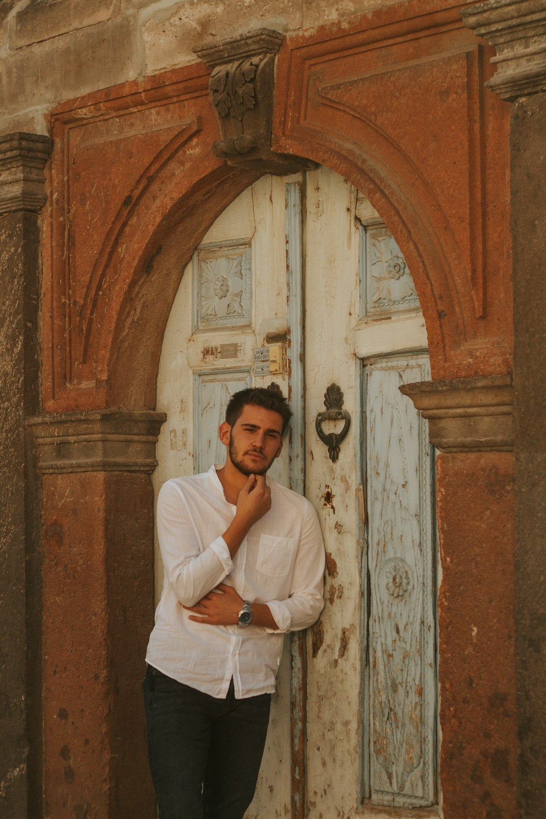 man in white dress shirt leaning on brown wooden door