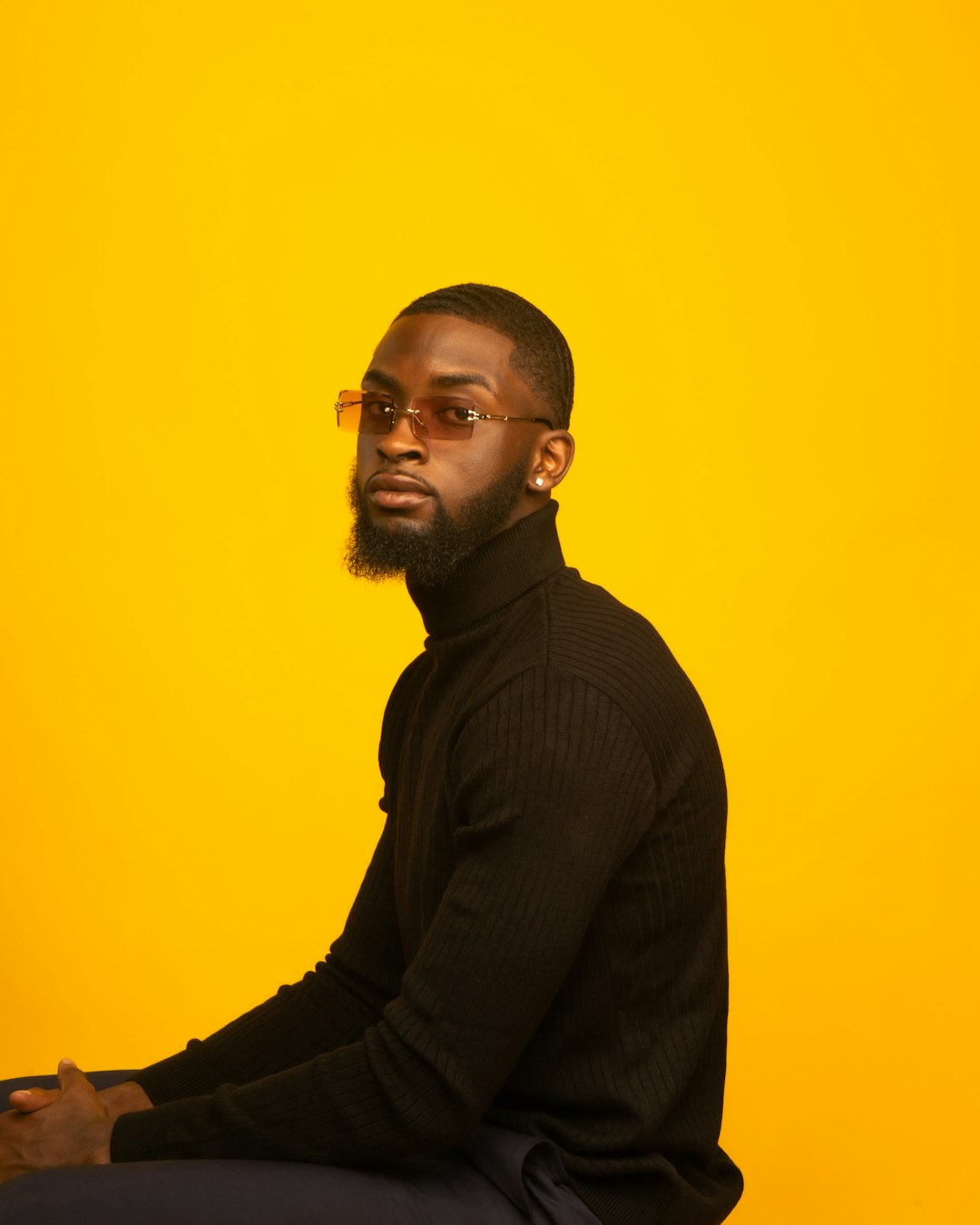 man in black sweater standing beside yellow wall