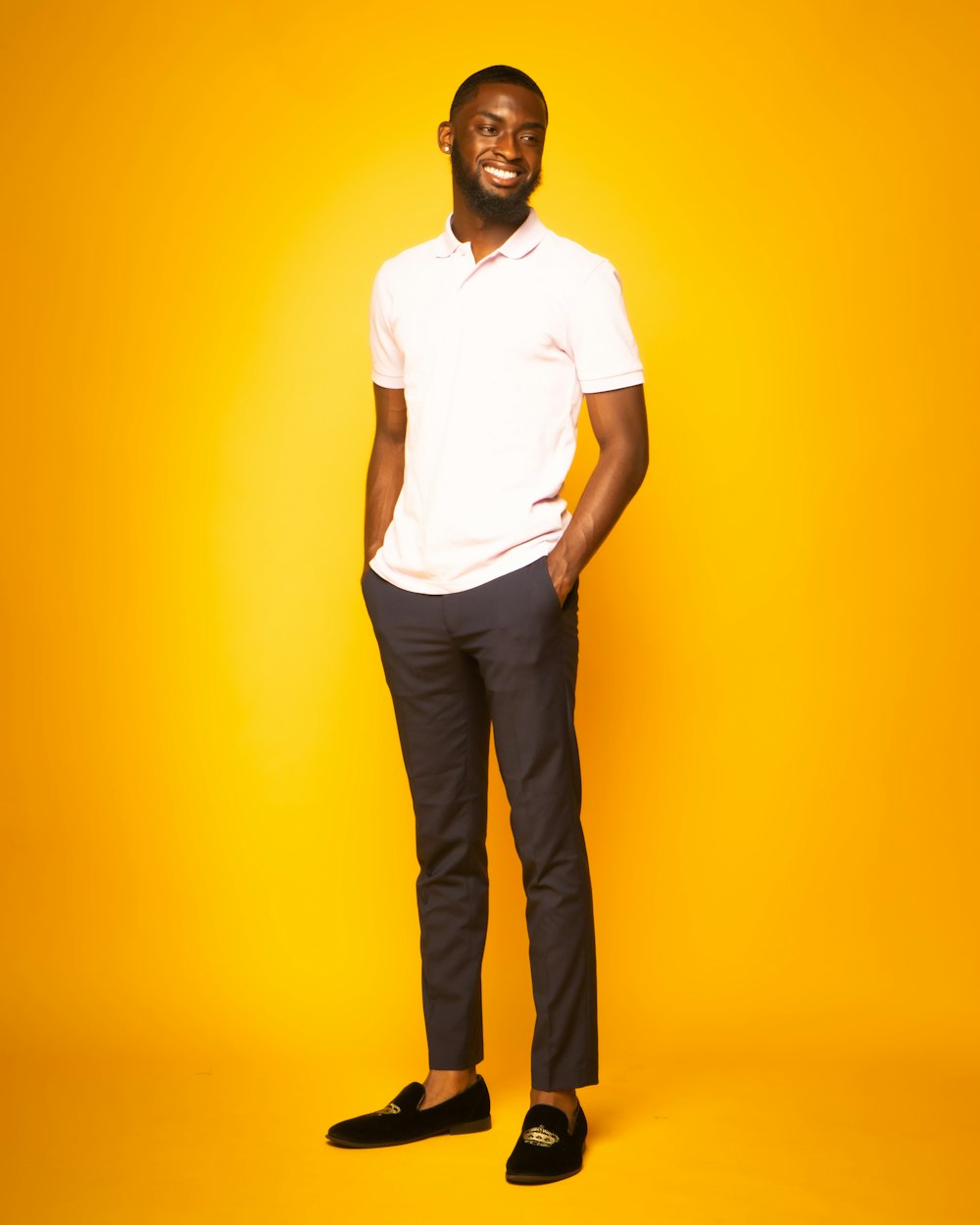 man in white button up shirt and black pants standing beside yellow wall