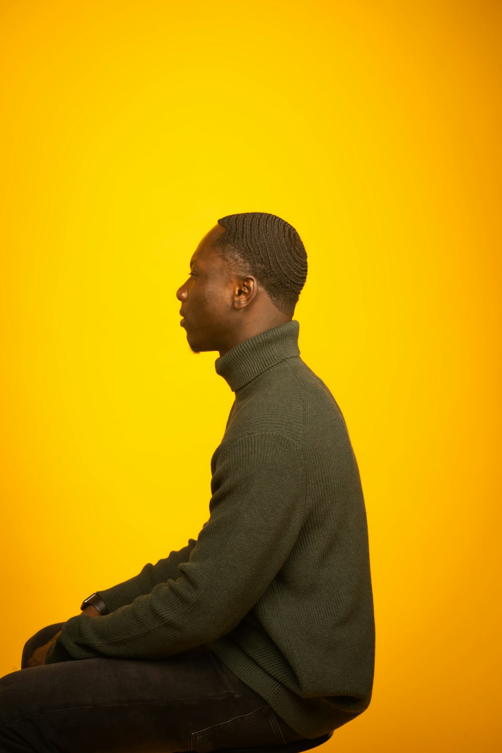 man in gray sweater standing beside yellow wall