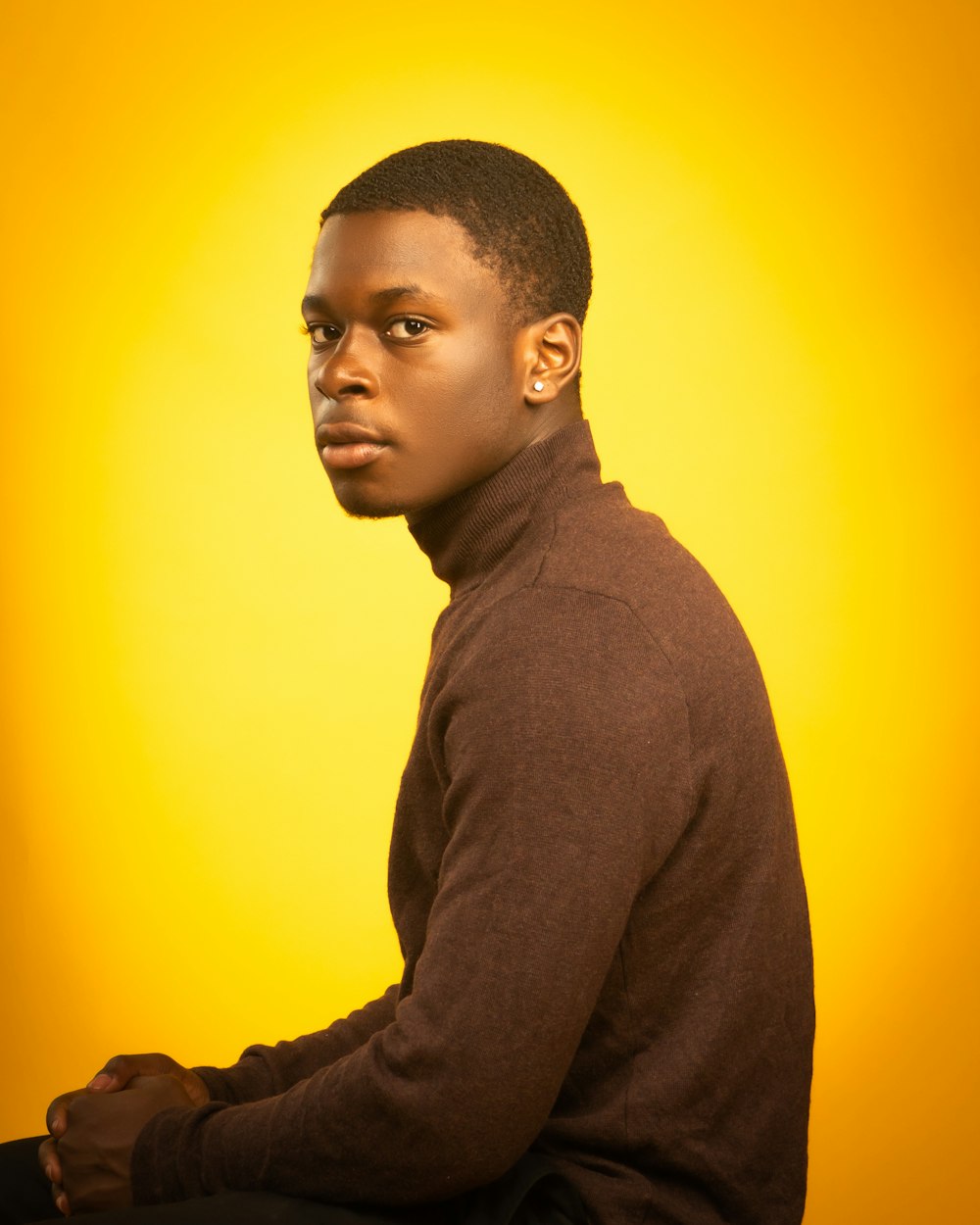 man in gray hoodie standing near yellow wall