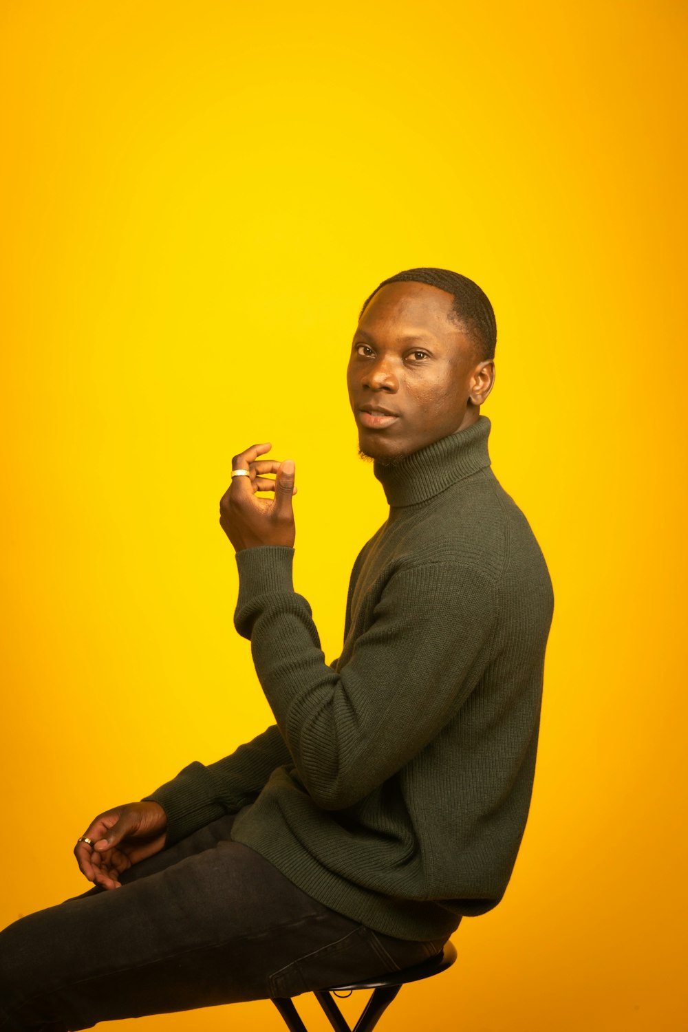 man in gray turtleneck sweater sitting beside yellow wall