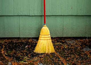 yellow broom leaning on white wall