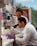 Two scientists in white lab coats are working in a laboratory, with one looking through a microscope and the other observing. The lab is equipped with various scientific equipment and supplies, including test tubes, a pipette, and laboratory storage shelves filled with containers and papers.