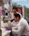 Two scientists in white lab coats are working in a laboratory, with one looking through a microscope and the other observing. The lab is equipped with various scientific equipment and supplies, including test tubes, a pipette, and laboratory storage shelves filled with containers and papers.
