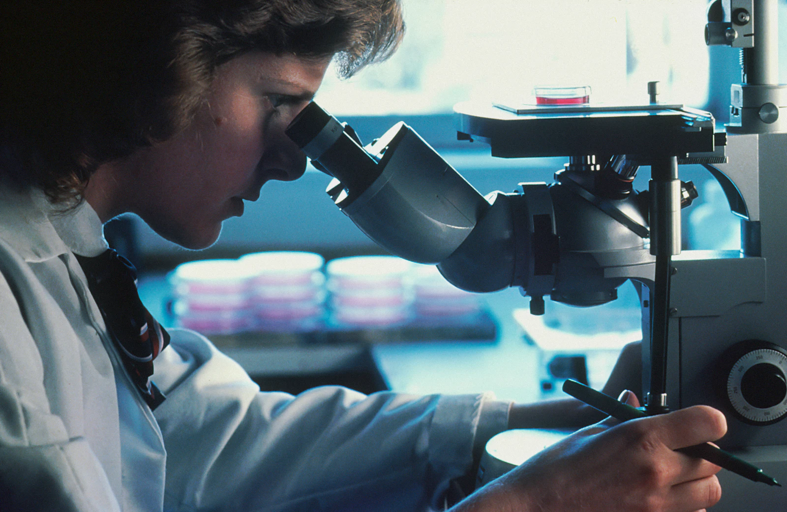 A person in a white lab coat looking through a microscope