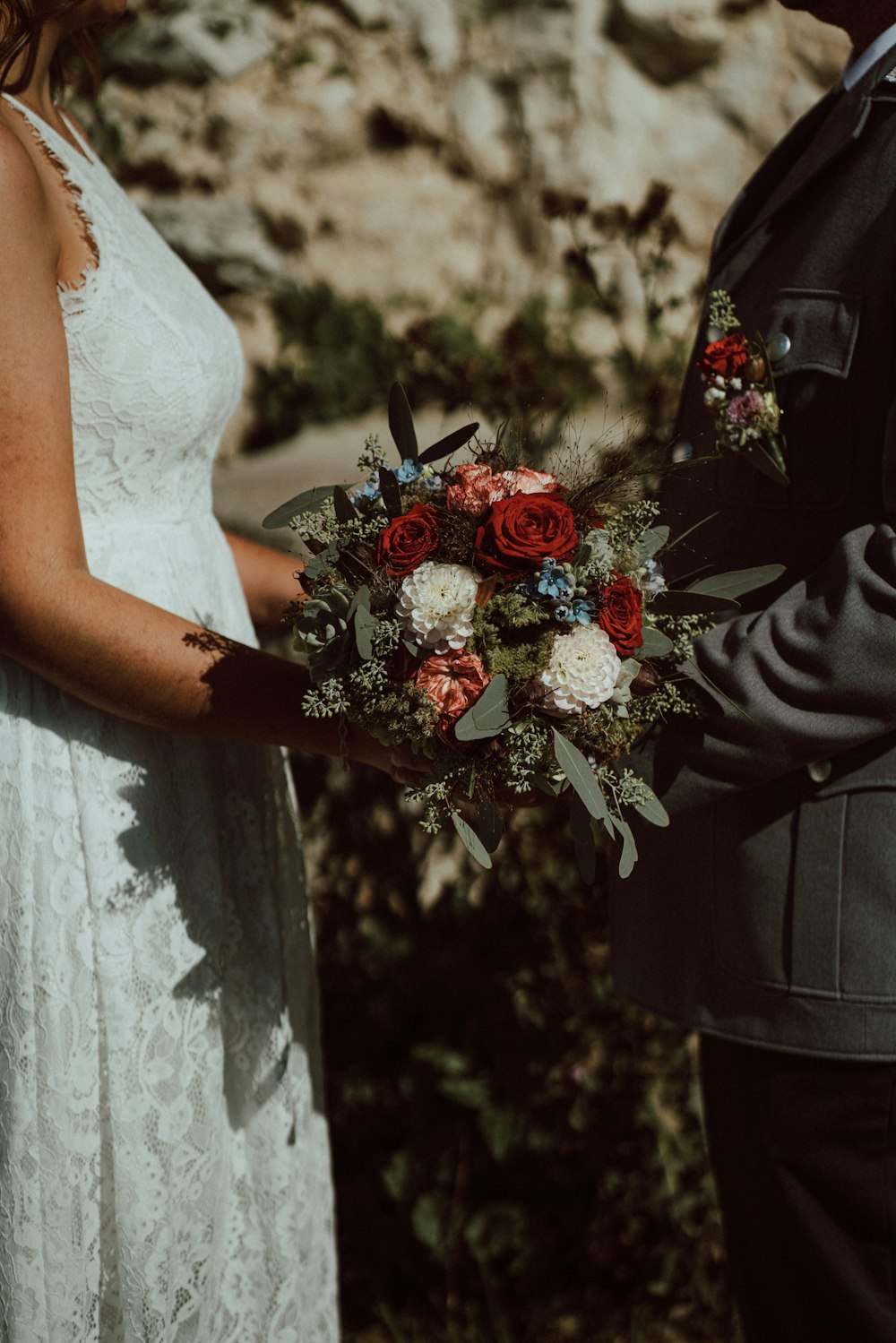 mujer en vestido de novia blanco sosteniendo ramo de rosas rojas