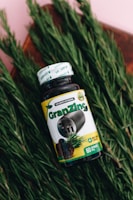 A bottle of dietary supplement labeled 'GranZinc' is placed on a bed of fresh green rosemary leaves. The label on the bottle includes the element symbol for zinc and pictures of rosemary and what appears to be a nut or seed.