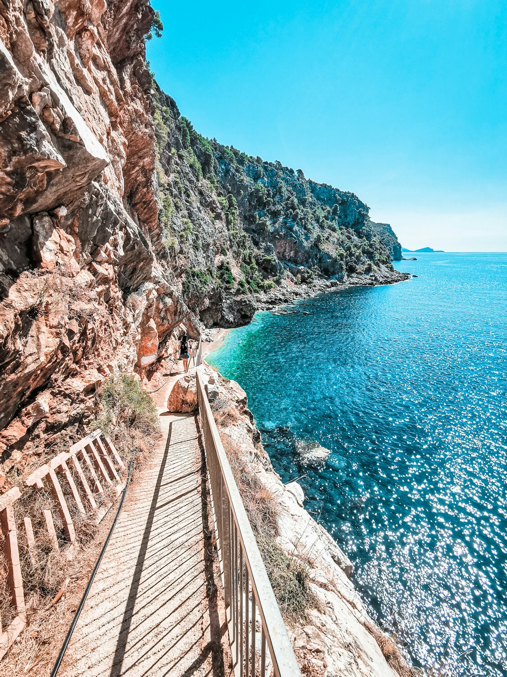 brown wooden bridge on rocky mountain near body of water during daytime